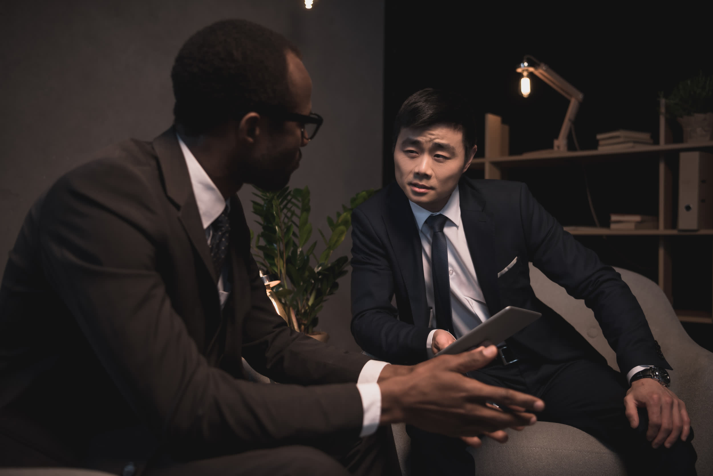 Two consultants in suits talking during a meeting in a dimly lit office