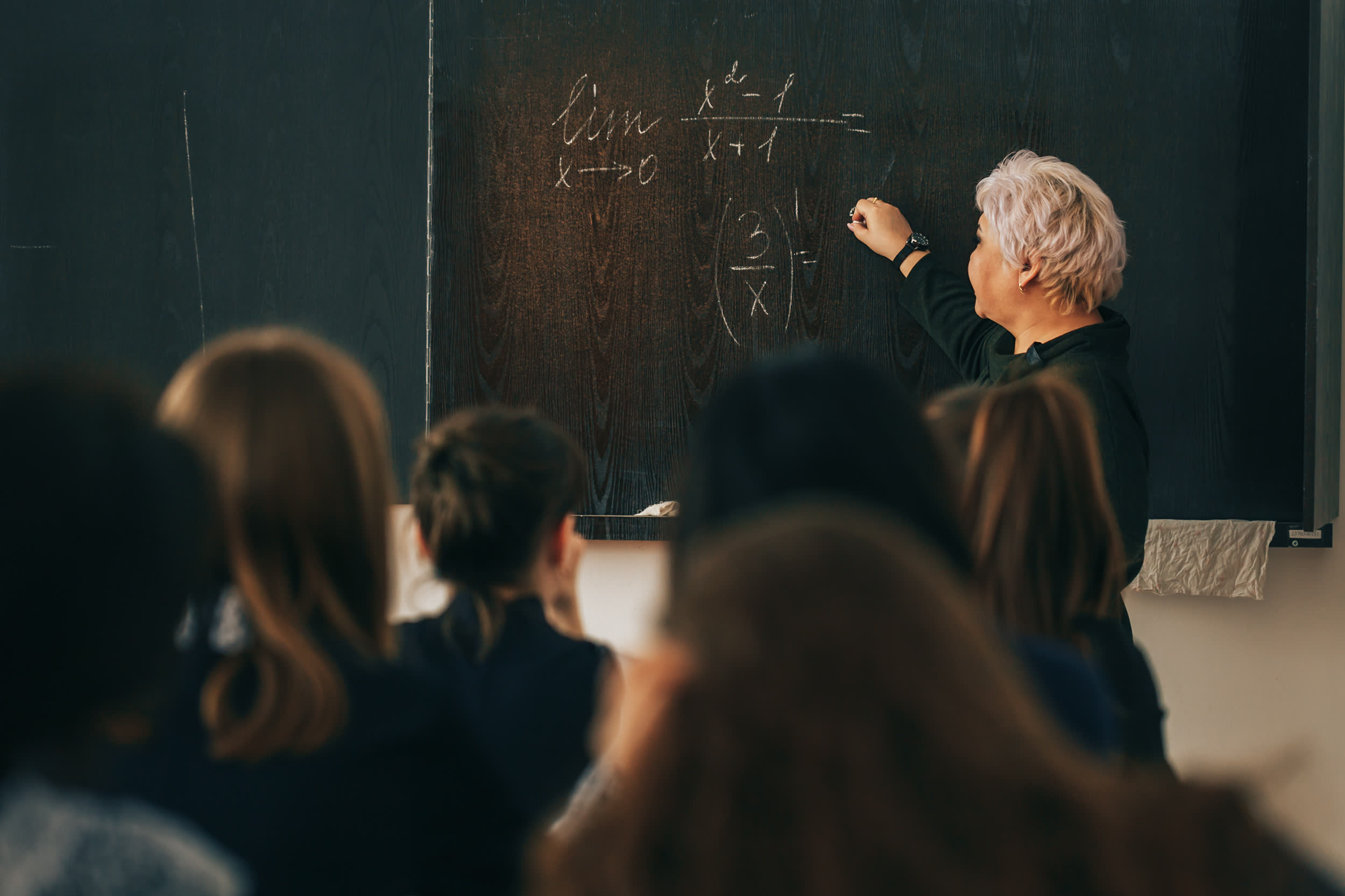 Lecturer writing on a blackboard in front of a class in a dark lecture room