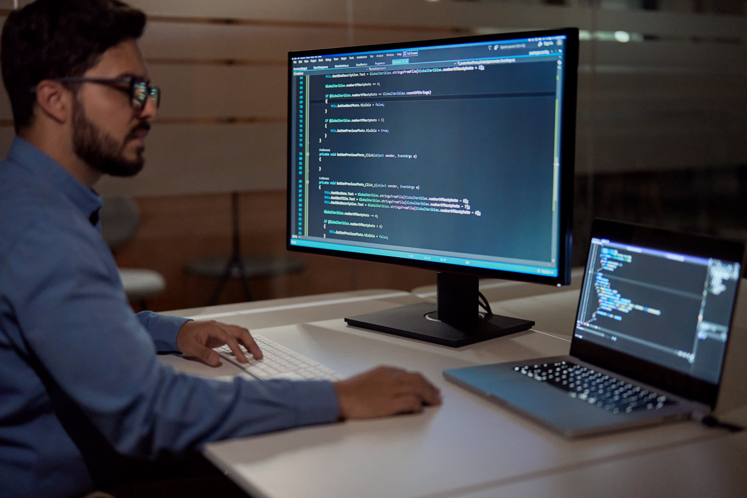 Developer typing code at a desk with two screens in a dimly lit office