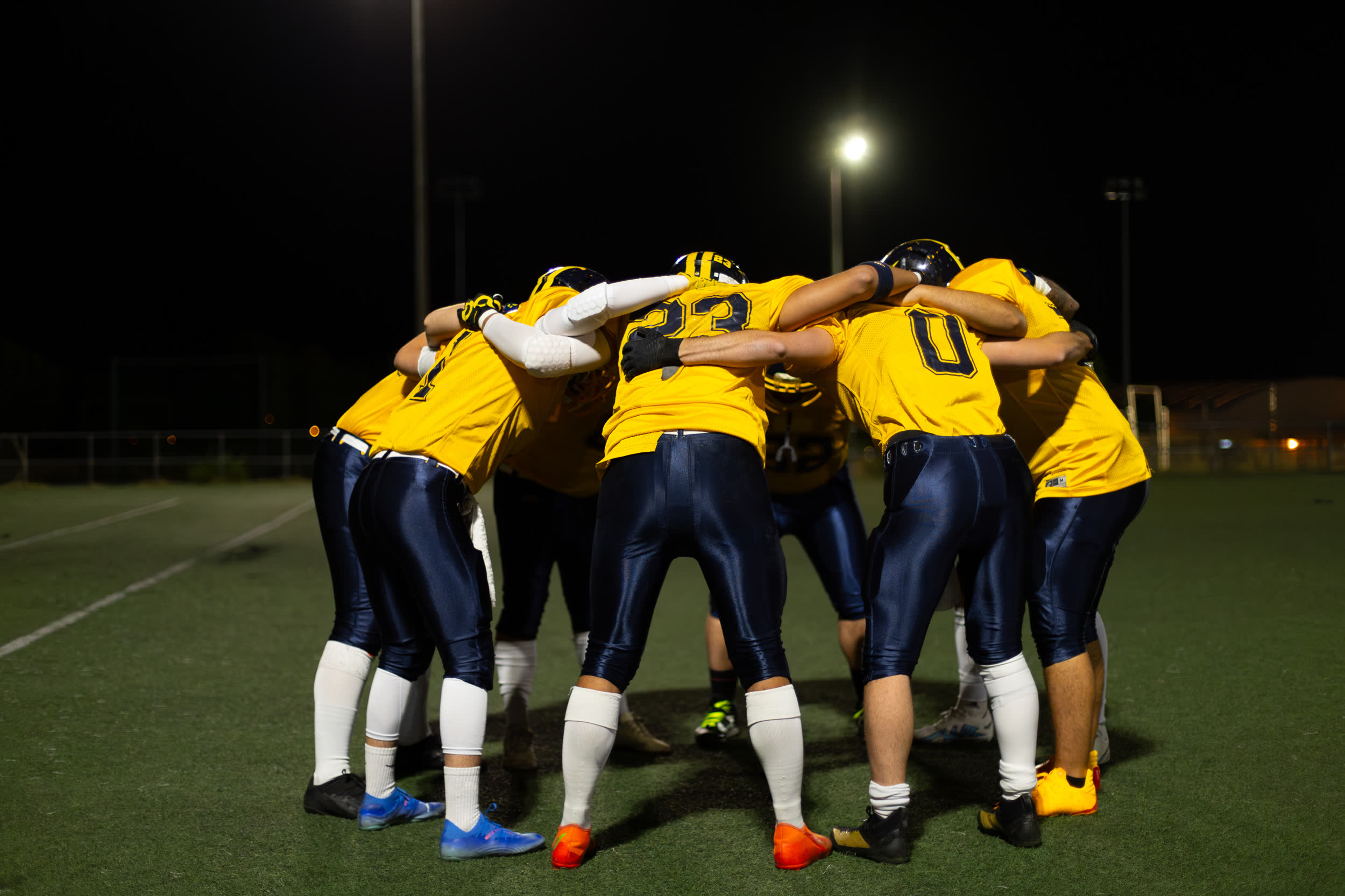 Sports team in a huddle on a pitch under floodlights at night
