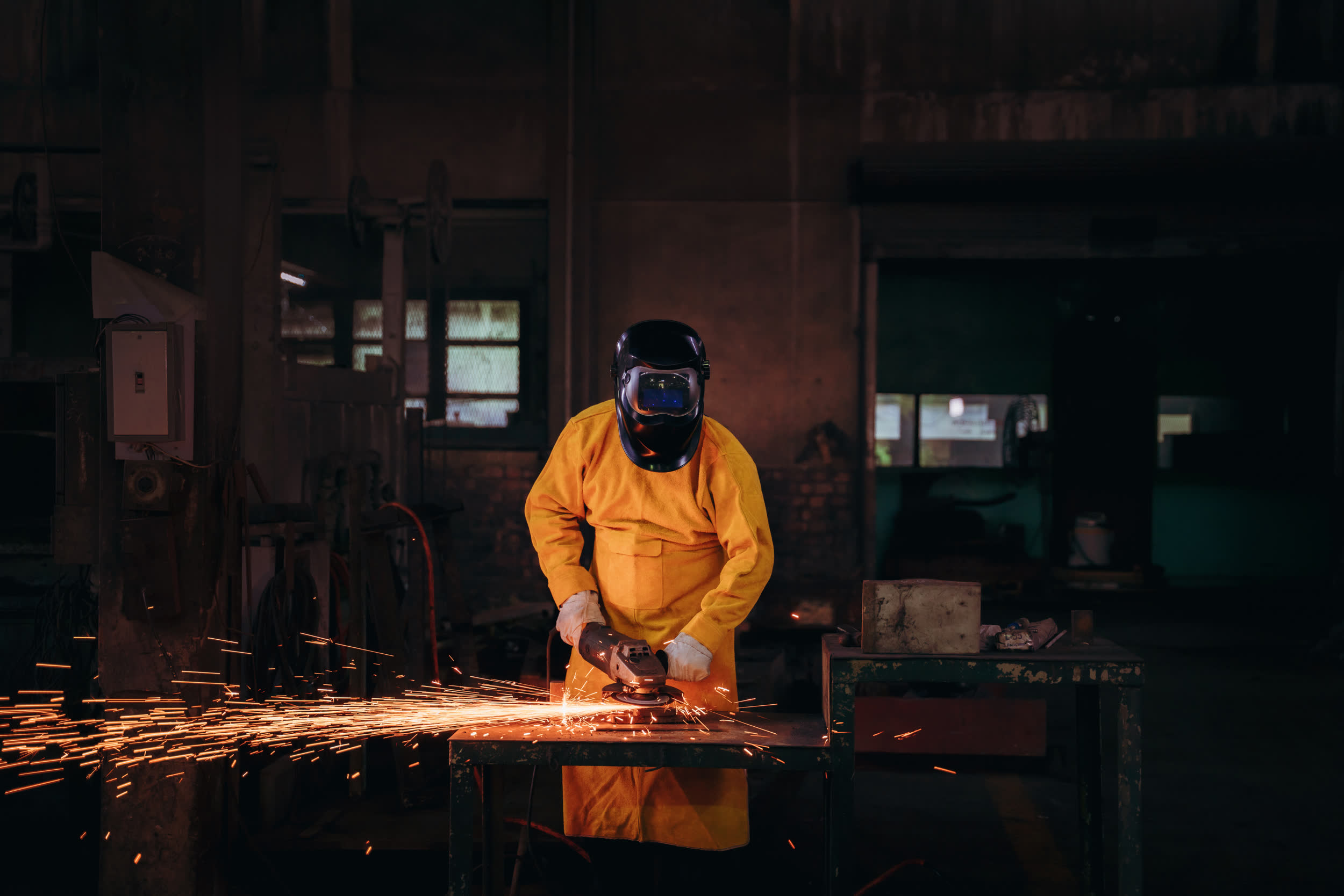 Welder grinding metal with sparks flying in a dark workshop
